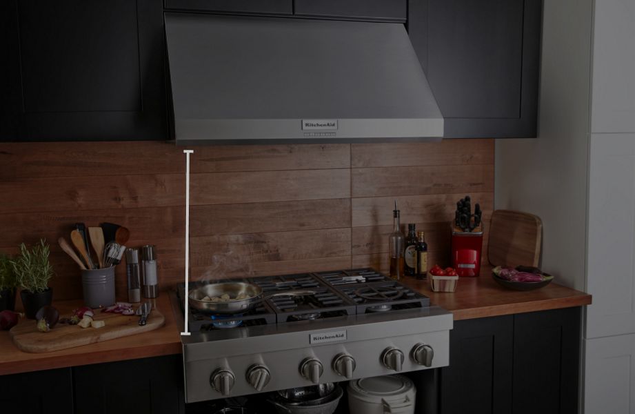 KitchenAid® wall-mount hood above gas range with food cooking in pan, featuring animated height measurement overlay.