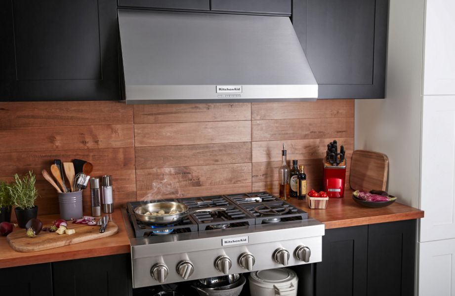 KitchenAid® wall-mount hood above gas range with food cooking in pan, featuring animated height measurement overlay.