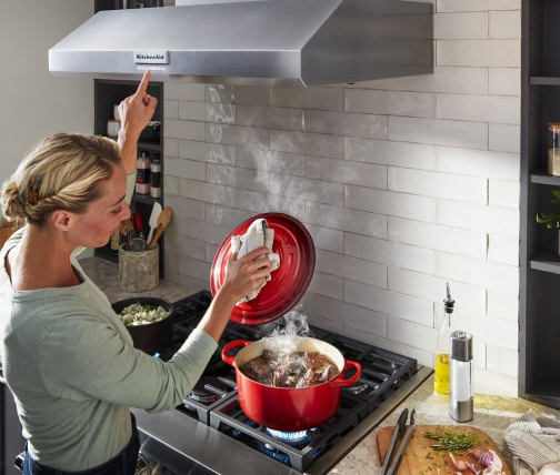 Woman cooking on a gas cooktop and turning on the wall mount hood