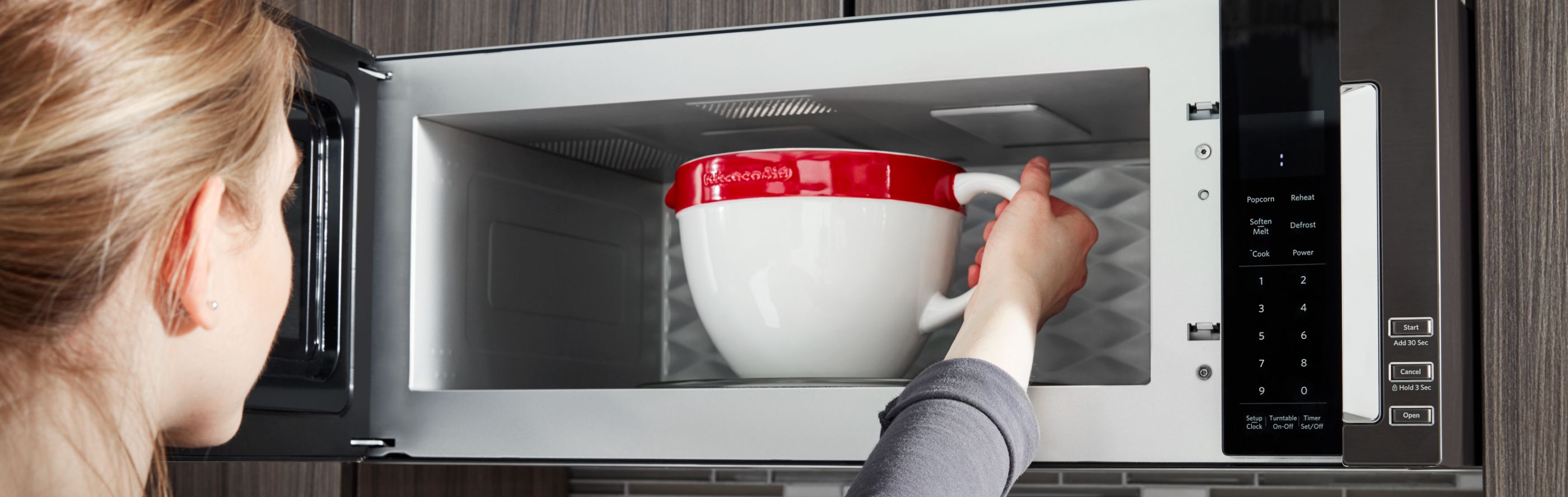 A woman placing a bowl in a KitchenAid® microwave.