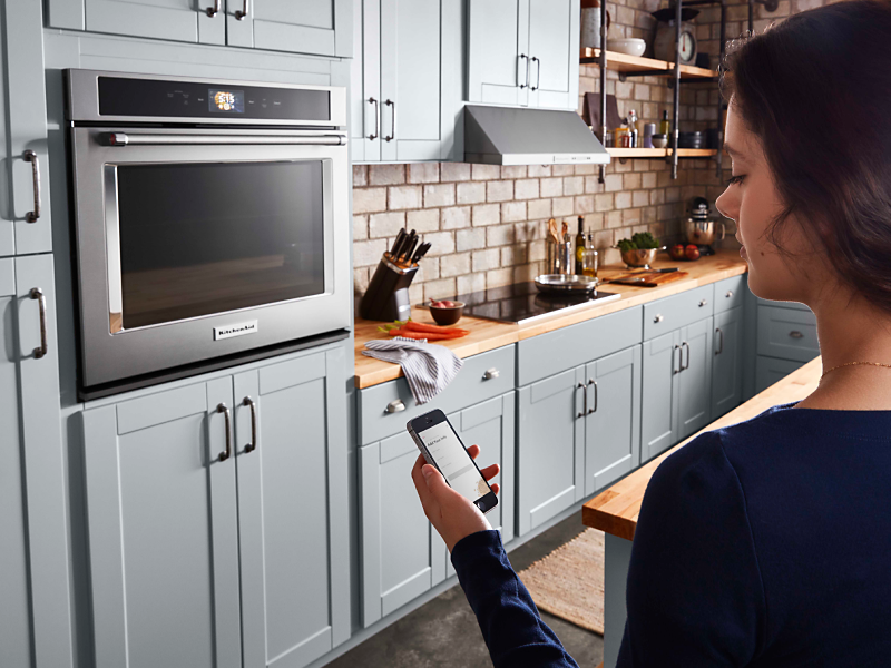 A woman checking a smartphone to control a smart oven
