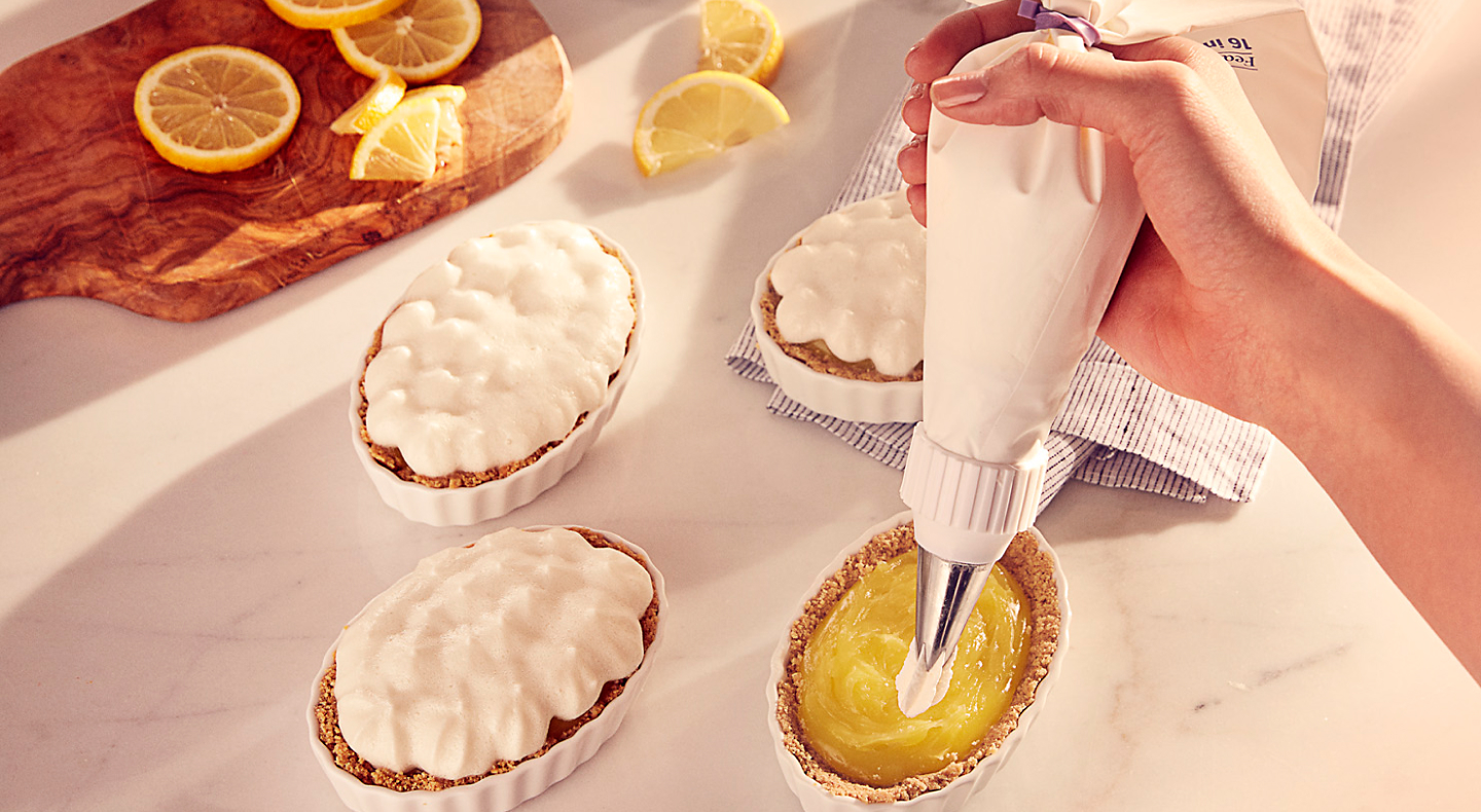 Person piping cream onto mini pies