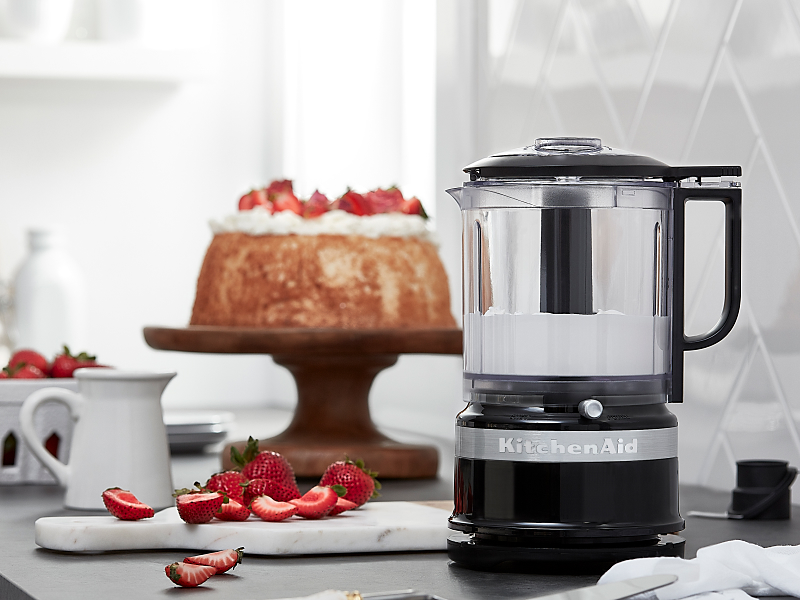Whipped cream in KitchenAid® food processor next to strawberries