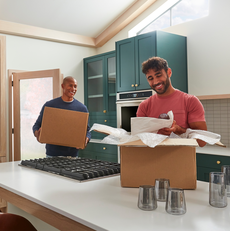 Two men moving and unpacking boxes in a remodeled kitchen.