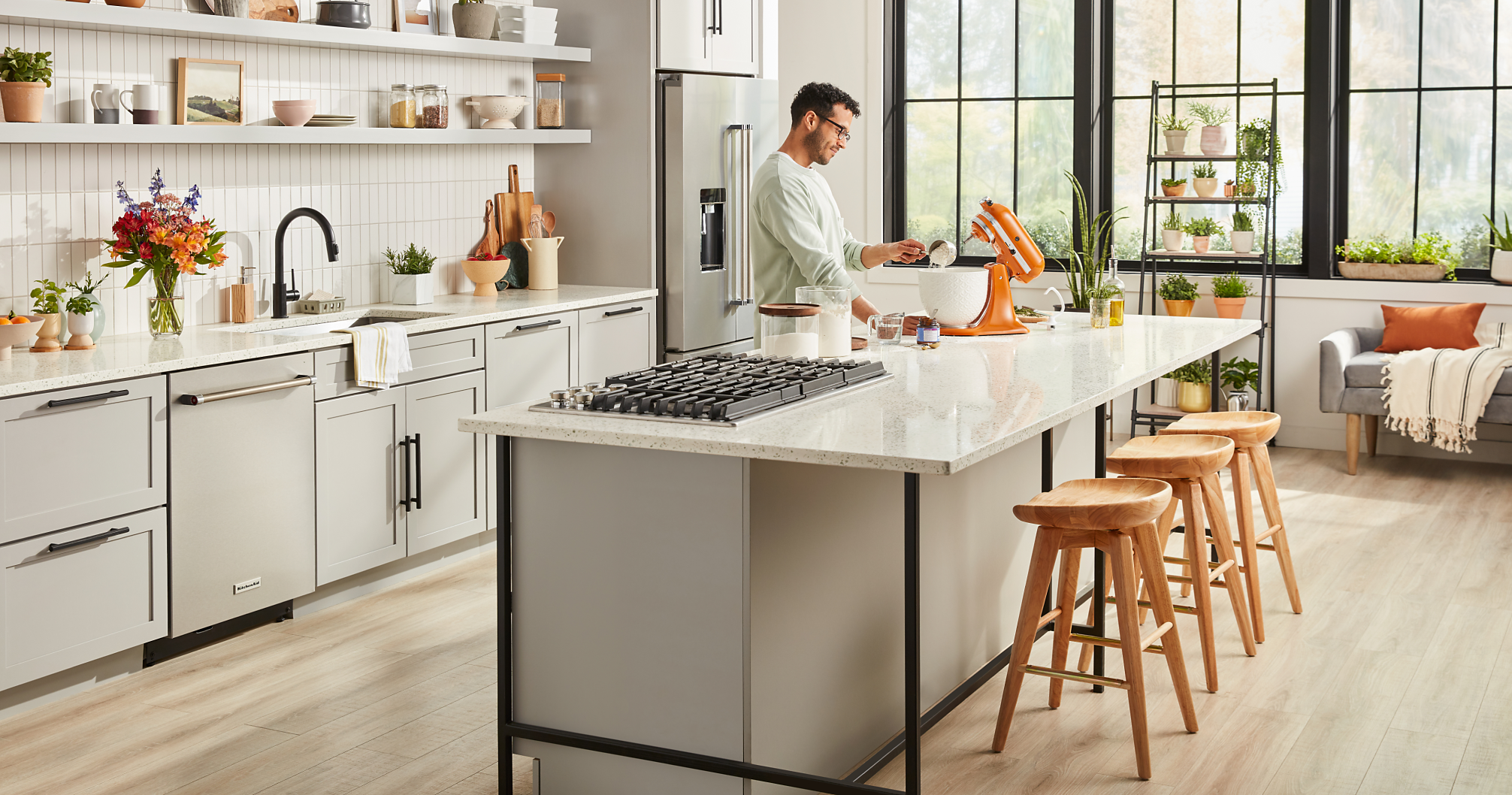 A man using a Honey KitchenAid® Stand Mixer on the island in a bright kitchen.