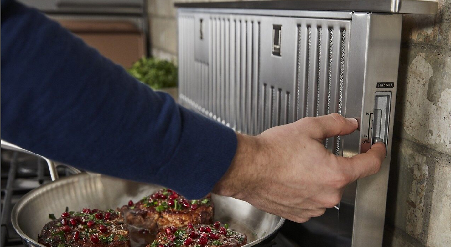 Man turning on a downdraft vent while food cooks on the stove