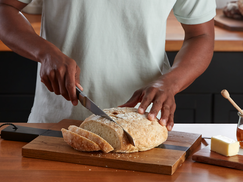 A person slicing bread next to an orange KitchenAid® stand mixer