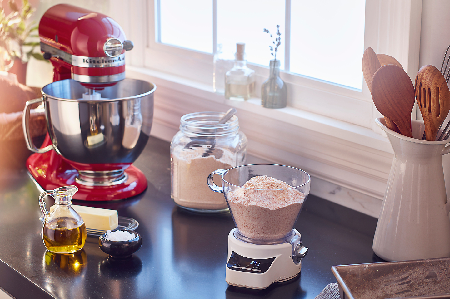 A red KitchenAid® stand mixer amongst a food scale and various baking ingredients