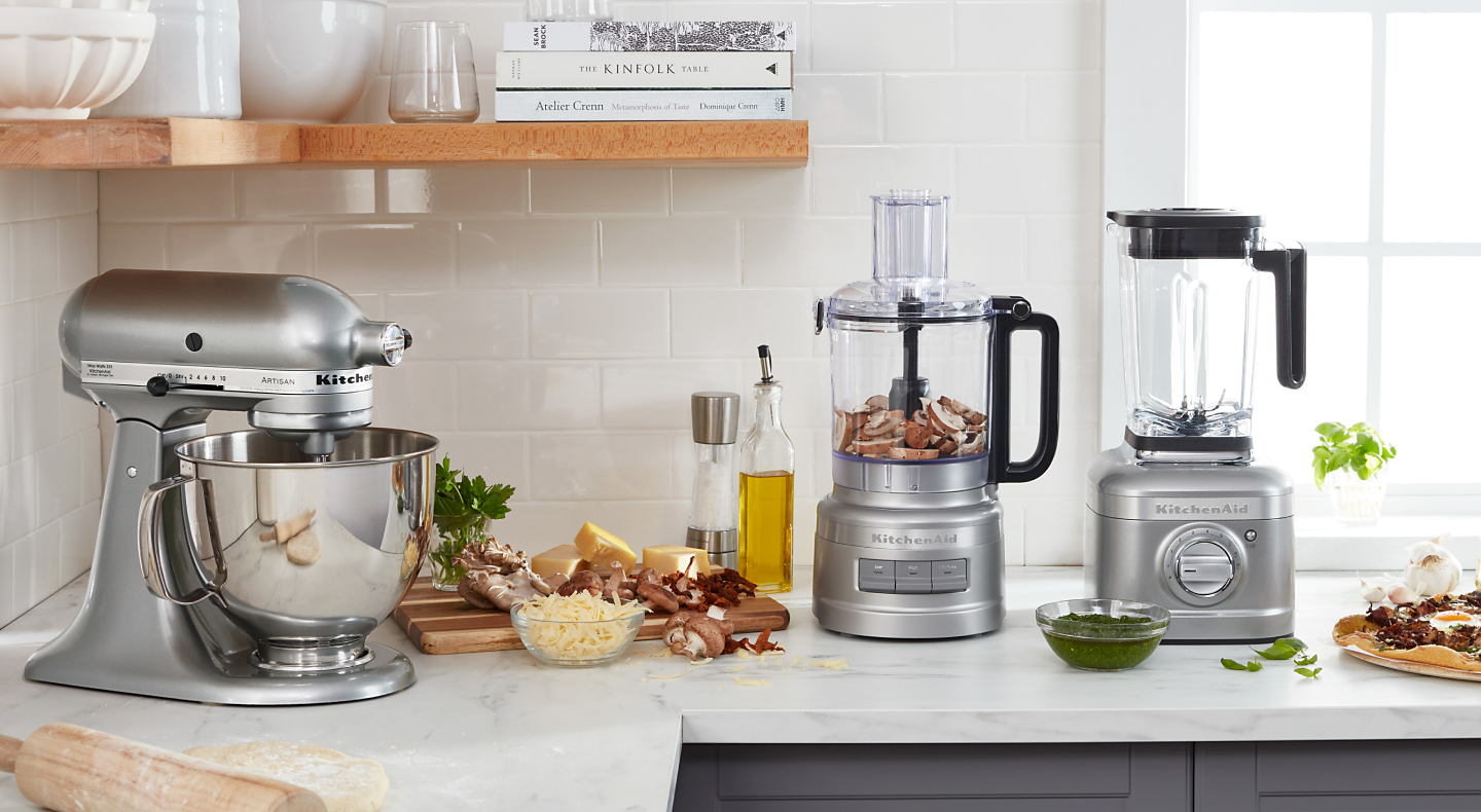 Silver KitchenAid® stand mixer, food processor and blender on counter next to prepared ingredients