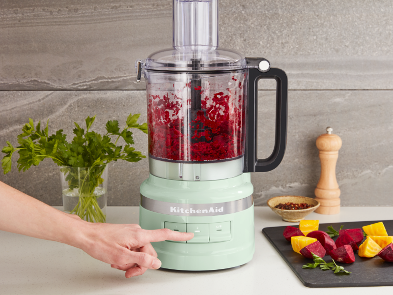 Person pulsing ingredients in a mint green KitchenAid® food processor