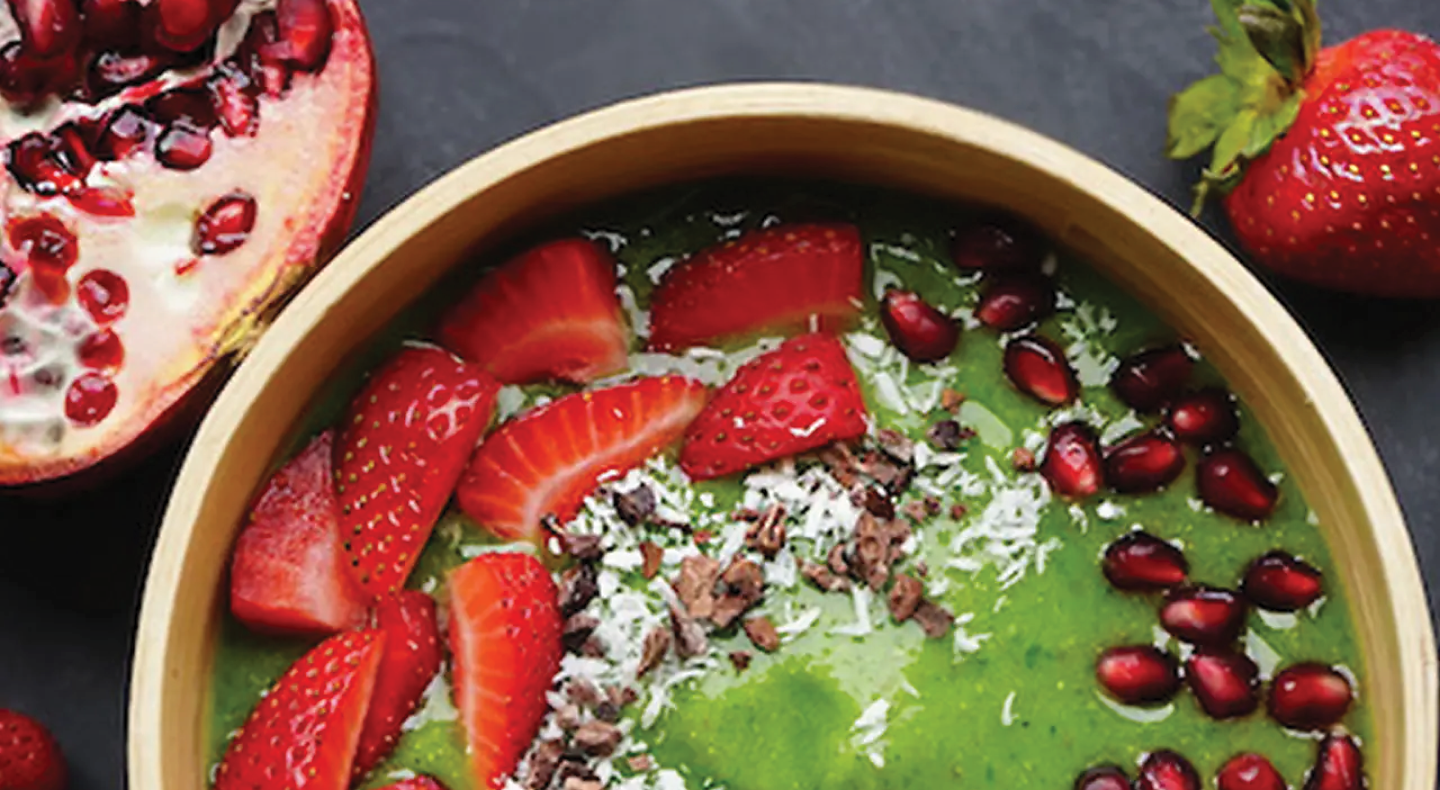 Close-up of green smoothie bowl with strawberries and pomegranate seeds