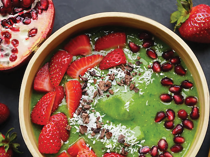 Close-up of green smoothie bowl with strawberries and pomegranate seeds