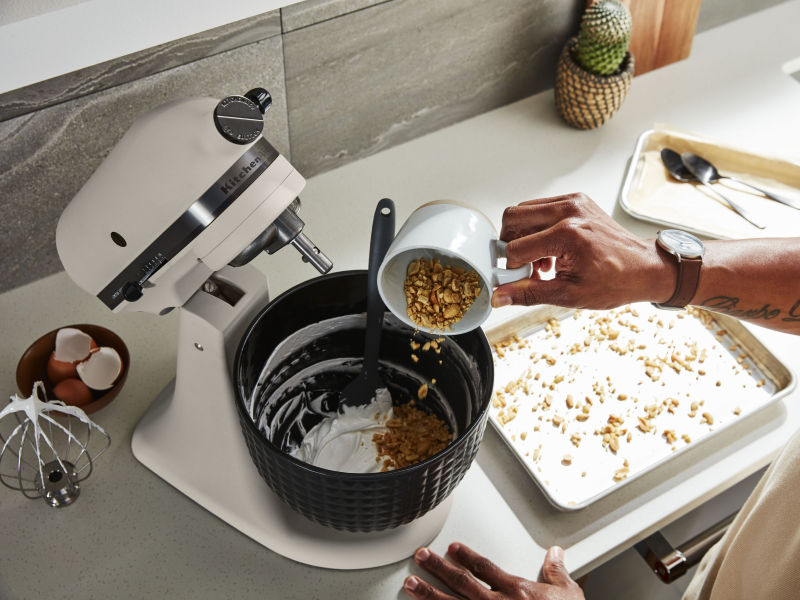 Person pouring ingredients into a white KitchenAid® stand mixer