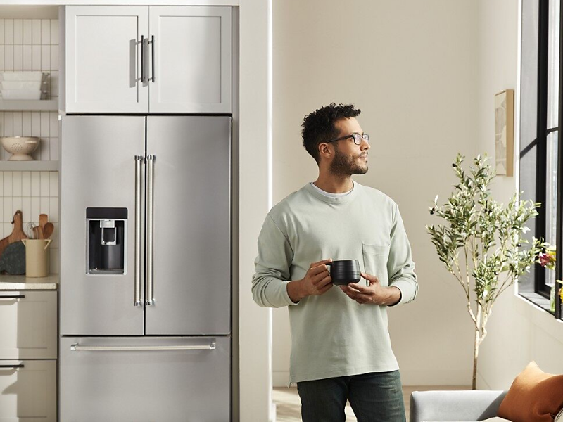Person with mug standing in front of stainless steel French-door refrigerator