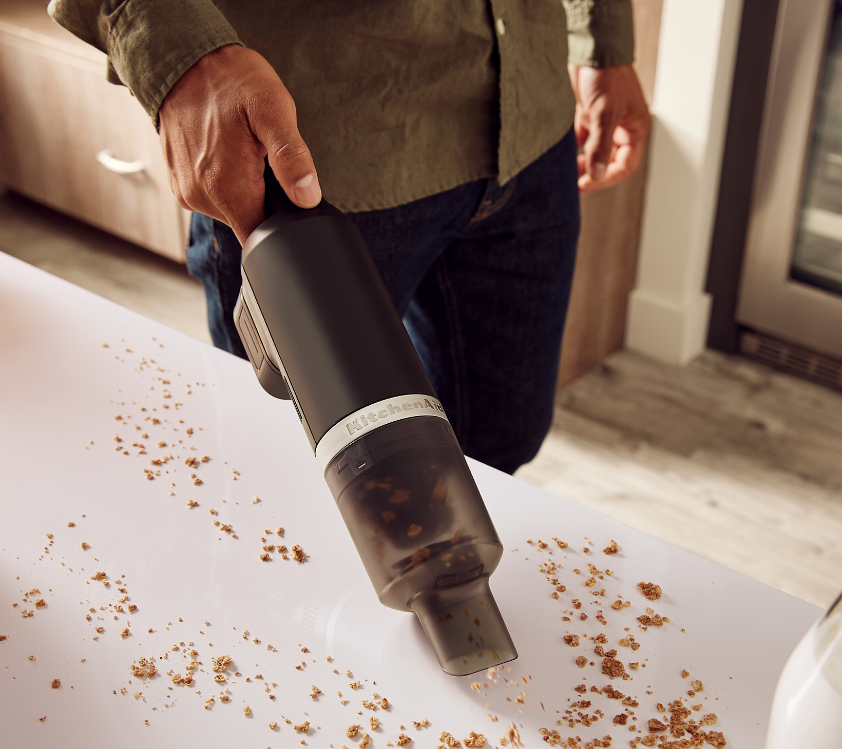 A person using the KitchenAid Go™ Cordless Kitchen Vacuum to pick up crumbs on a countertop.