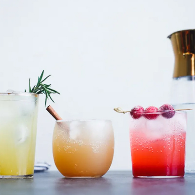 Three glasses of colorful mocktails with festive garnishes.