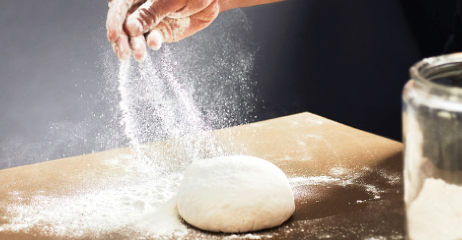 Hand sprinkling flour over a ball of dough