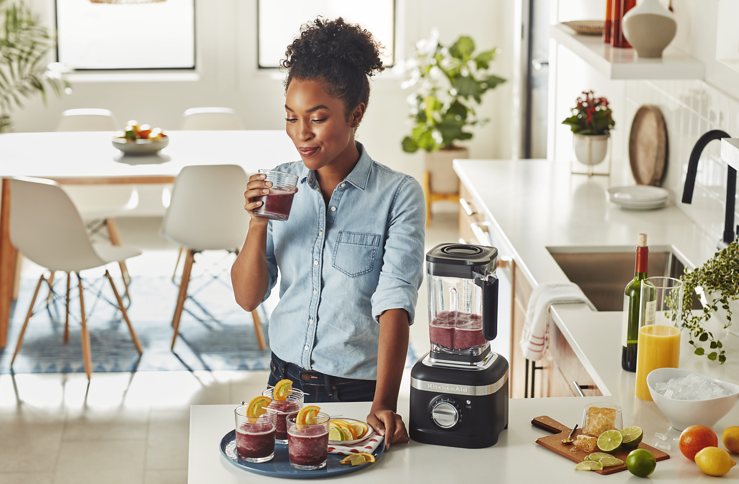 Person drinking a fruity beverage next to a KitchenAid® blender