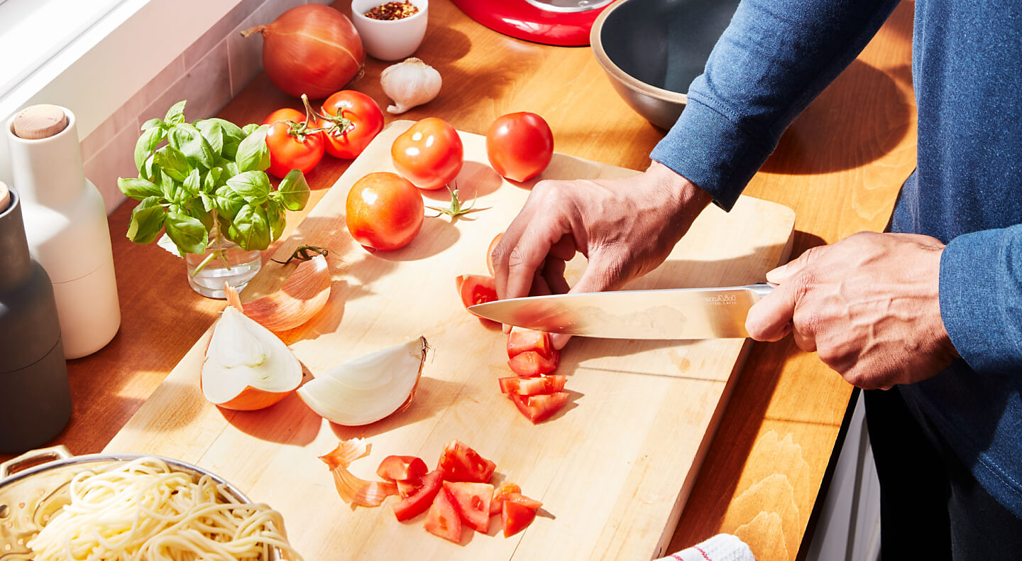 A person chopping tomatoes on a cutting board