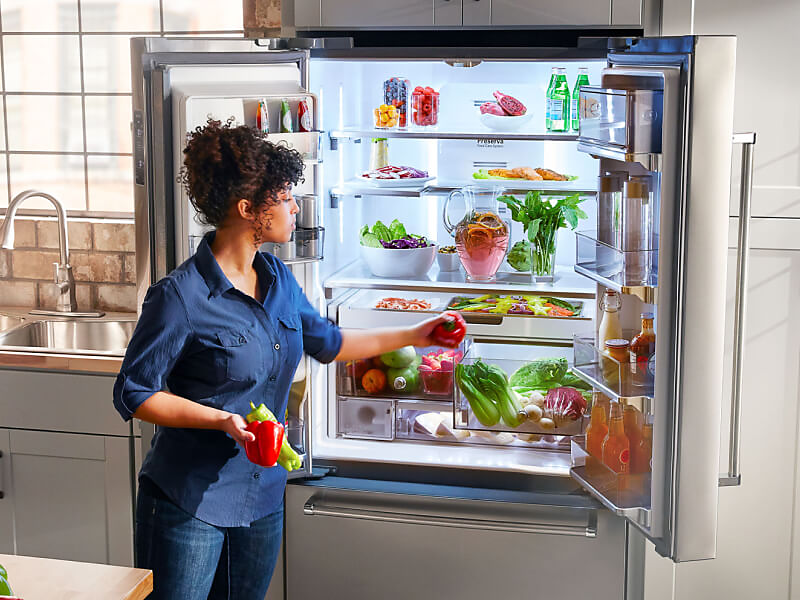 A person putting away fresh vegetables in a KitchenAid® french door refrigerator
