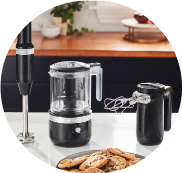 Matte Black KitchenAid® cordless immersion blender, food chopper, and hand mixer on white countertop.
