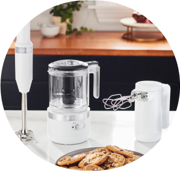 White KitchenAid® Cordless Immersion Blender, Food Chopper, and Hand Mixer on white countertop.
