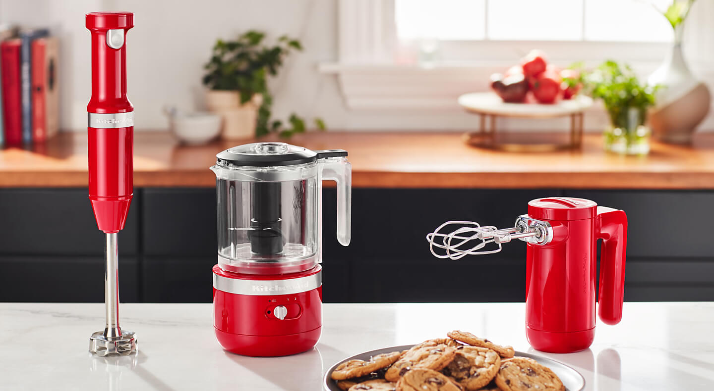 KitchenAid® red cordless hand blender, food chopper and hand mixer on a countertop