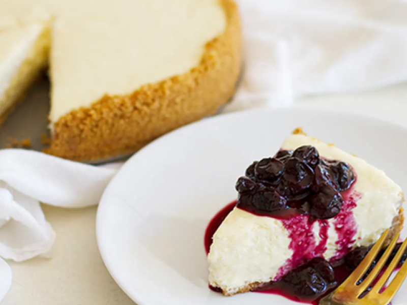 Slice of cheesecake on white plate with blueberry sauce
