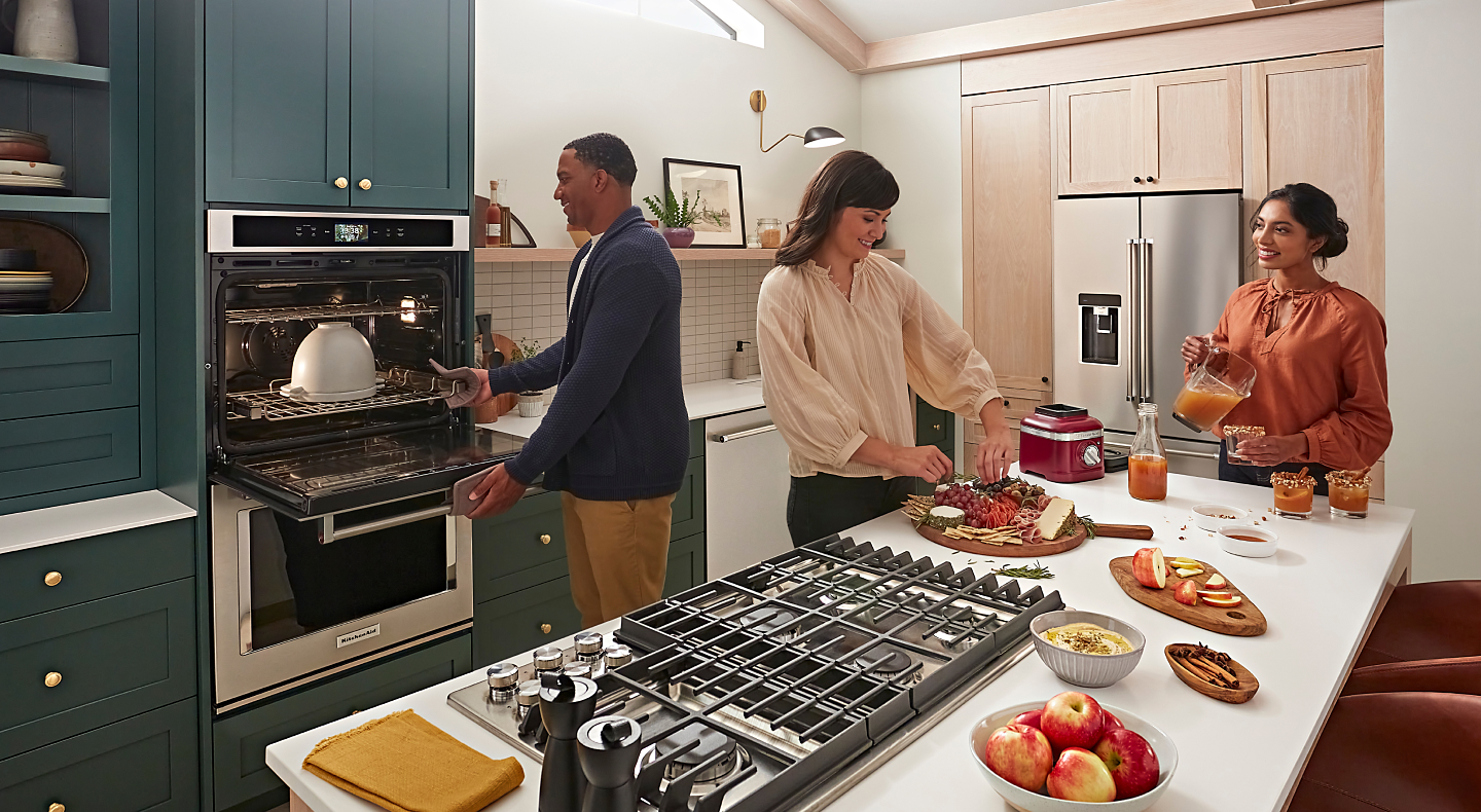 Man placing proofing bowl in oven as two women prepare drinks and appetizers on the island