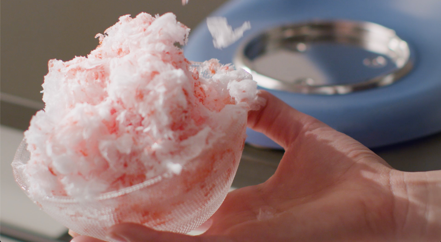 Hand holding bowl of shave ice dessert covered in pink syrup