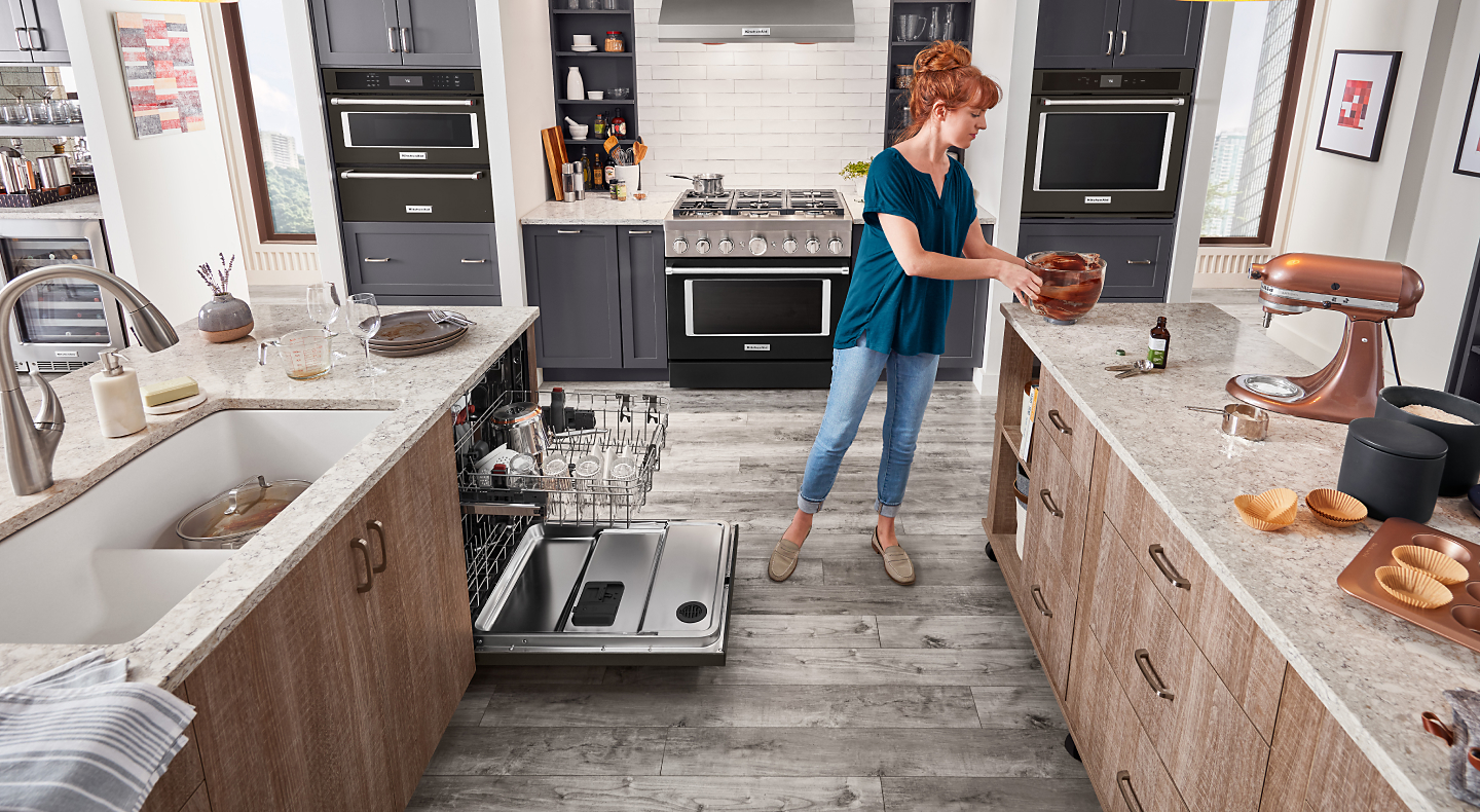 A KitchenAid® stand mixer on the counter with a person about to place the stand mixer bowl in the dishwasher.