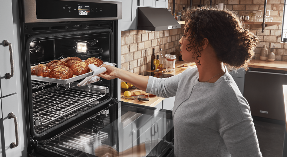 Woman removing fresh-baked croissants from oven