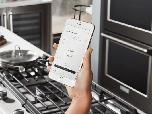 Hand holding a smartphone connected to a KitchenAid® smart oven