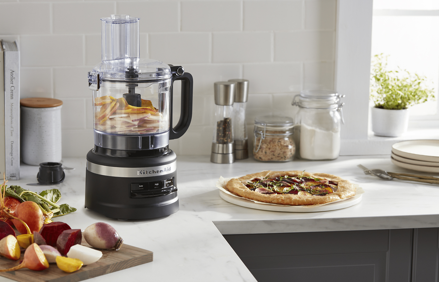A black KitchenAid® food processor next to a pizza on the counter.