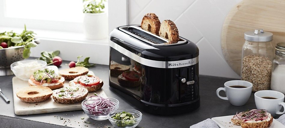 Bagels in a black toaster with topping ingredients on the counter Bagels in a black toaster with topping ingredients on the counter
