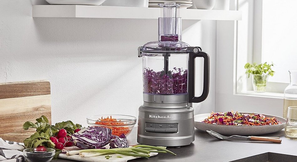 Silver food processor shredding red cabbage surrounded by vegetables Silver food processor shredding red cabbage surrounded by vegetables