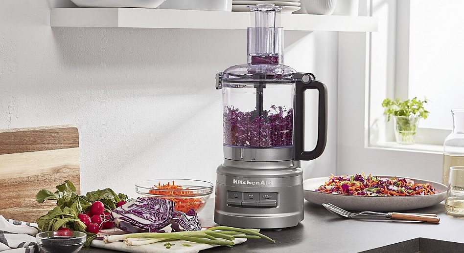 Silver food processor shredding red cabbage surrounded by vegetables