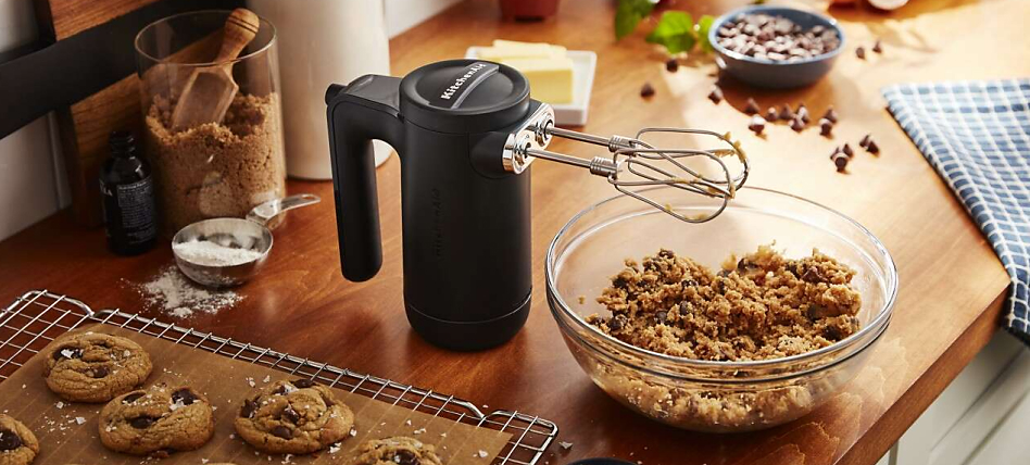 Black cordless hand mixer with cookie dough and baked cookies