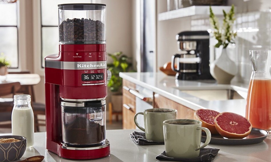 Red burr coffee grinder on counter with coffee cups and grapefruit Red burr coffee grinder on counter with coffee cups and grapefruit