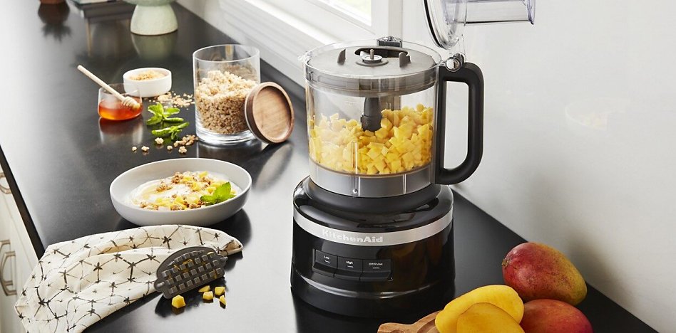 Black KitchenAid® food processor on a counter with chopped mango in the work bowl Black food processor on a counter with chopped mango in the work bowl