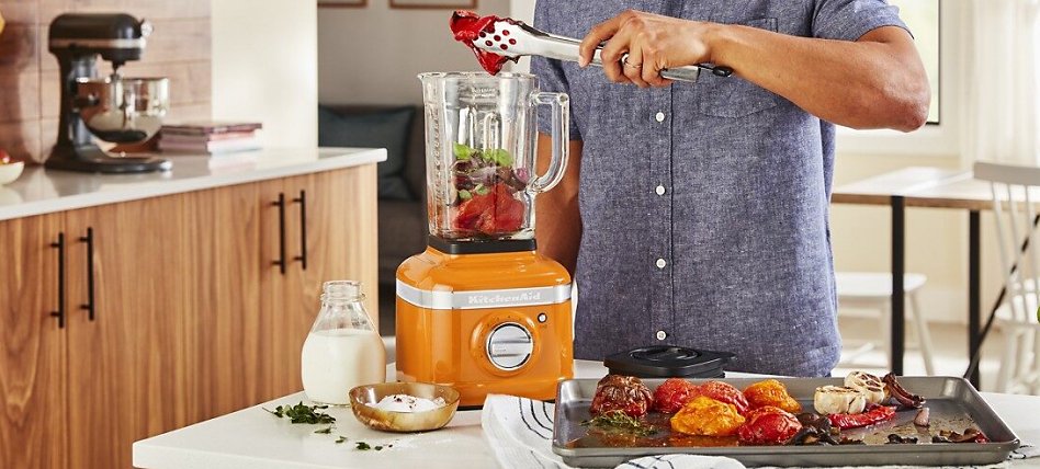 Man putting roasted vegetables into a Honey colored blender Man putting roasted vegetables into a Honey colored blender