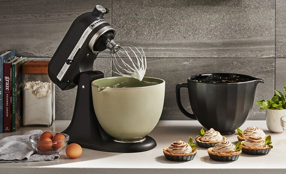 A black stand mixer on the counter with 4 ceramic mixing bowls.