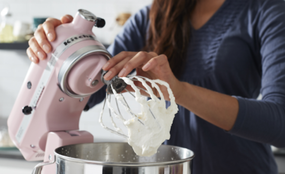 Woman removing whip attachment covered in whipped cream from pink stand mixer