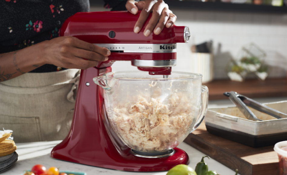 Woman operating a red stand mixer to shred chicken