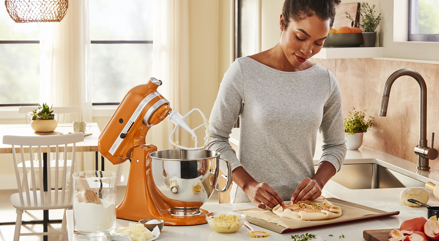 Person folding dough next to an orange KitchenAid® stand mixer