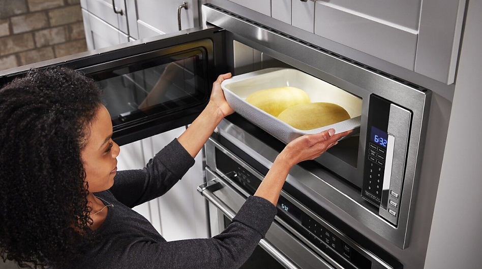 Woman sliding casserole dish inside built-in microwave