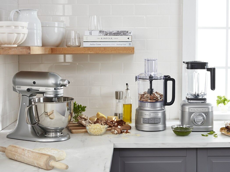 KitchenAid® stand mixer, food processor and blender on countertop with cutting board and ingredients