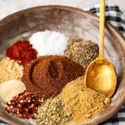A variety of spices in a brown ceramic bowl with a wooden spoon