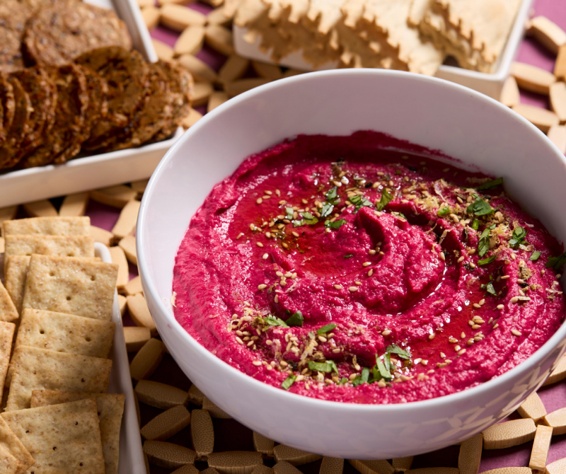 Beetroot hummus surrounded by an assortment of crackers