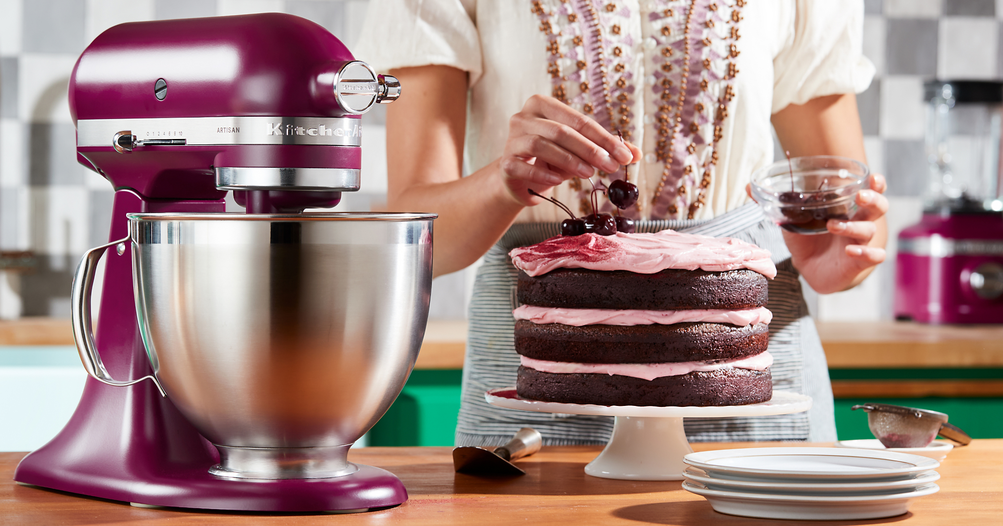 Woman garnishing chocolate layer cake with cherries placed next to KitchenAid® stand mixer in Beetroot